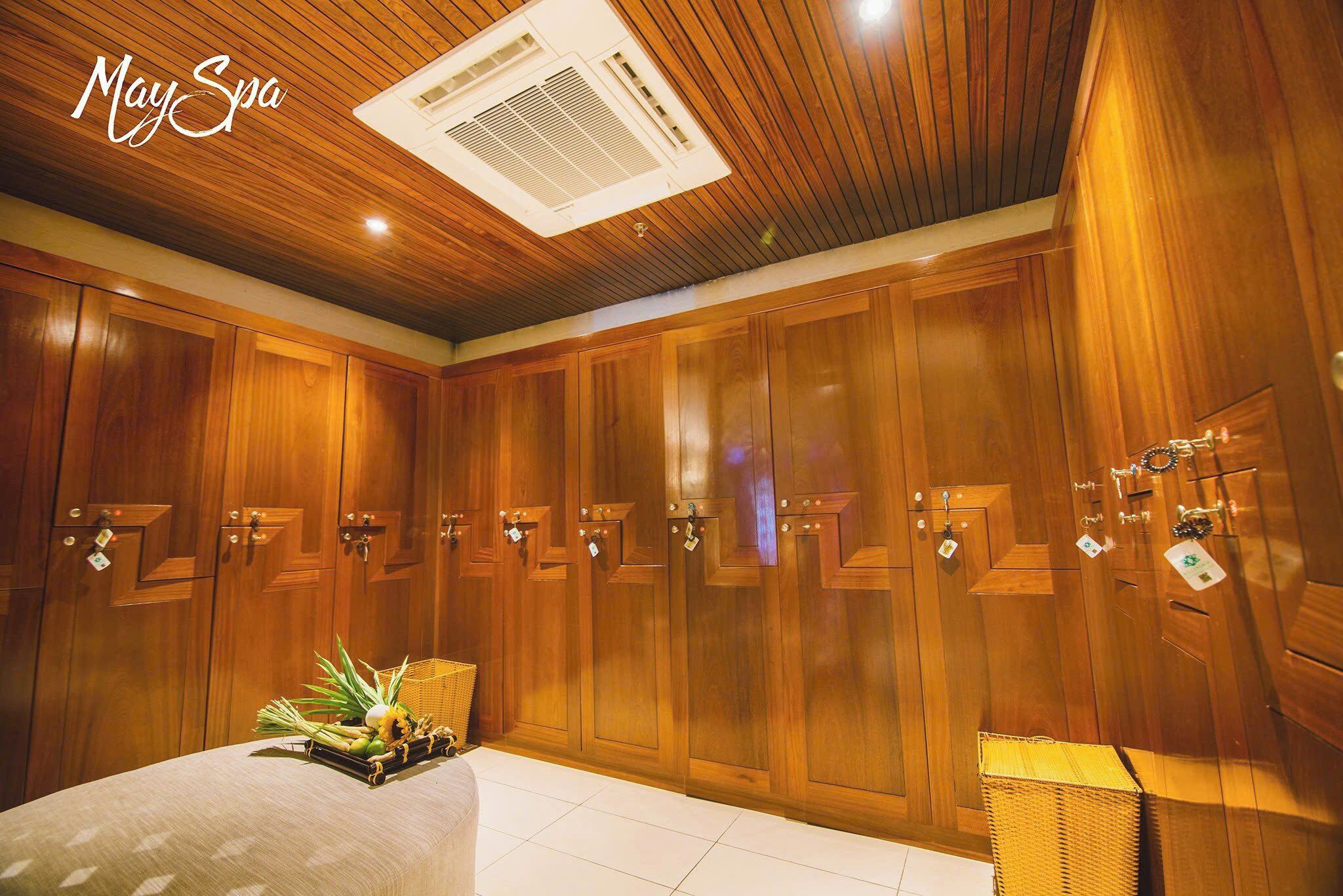 A spa room with wooden paneling, a ceiling air conditioner, and a bed with a decorative arrangement.
