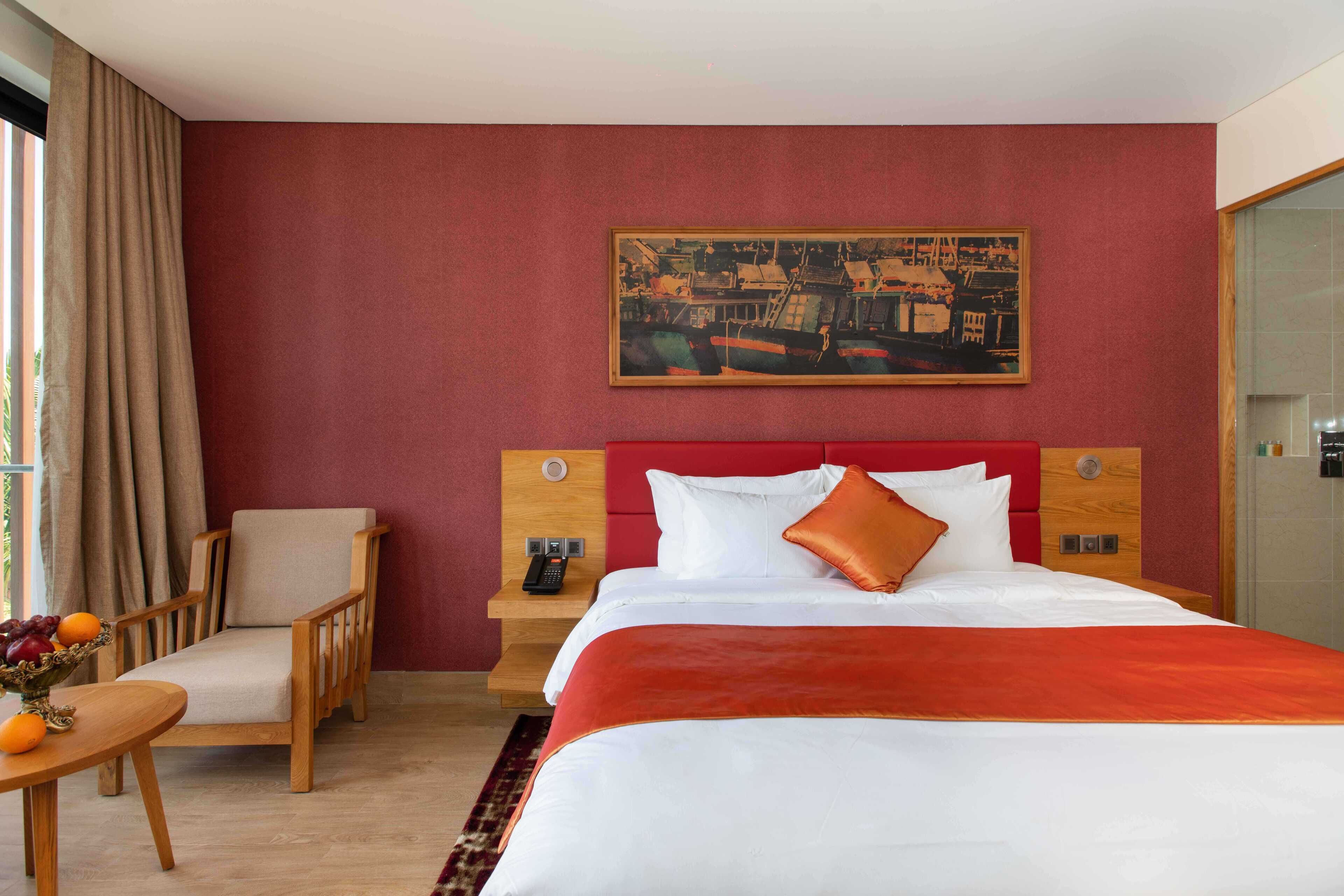 A hotel room with a bed, a chair, a nightstand, a painting, and a window with curtains.