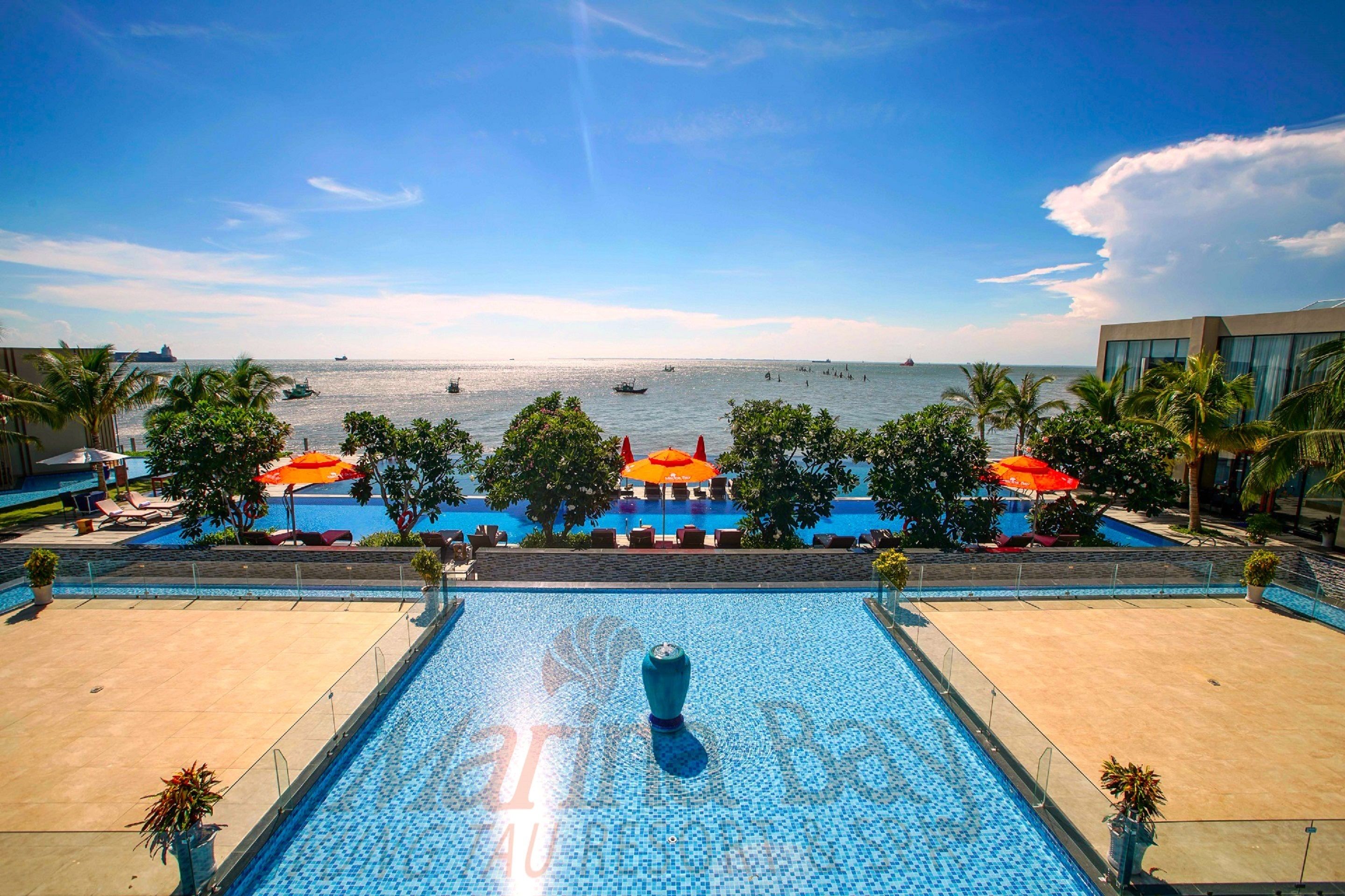 Piscina com vista para o mar, rodeada por palmeiras e espreguiçadeiras.