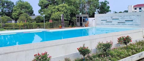 A swimming pool with a small structure, surrounded by greenery and a clear sky.