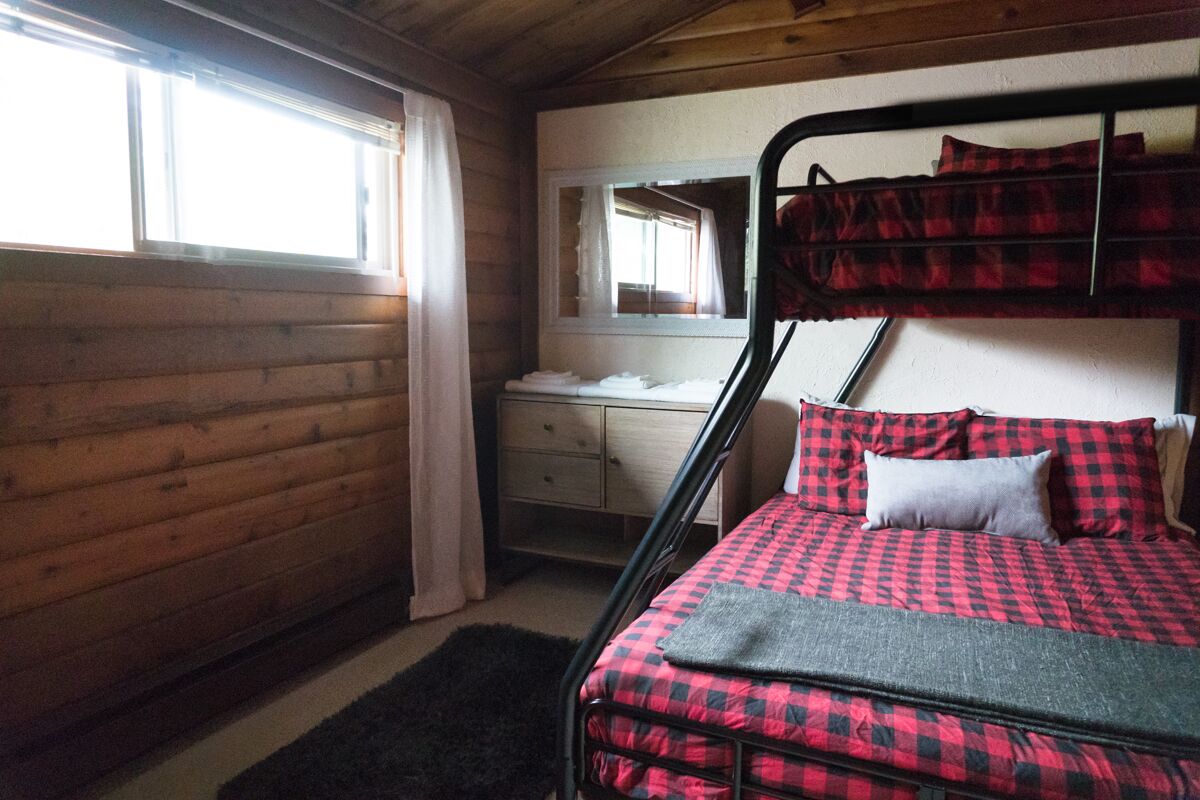 Un lit superposé avec une couverture à carreaux, une table de chevet avec un miroir et une commode en bois.