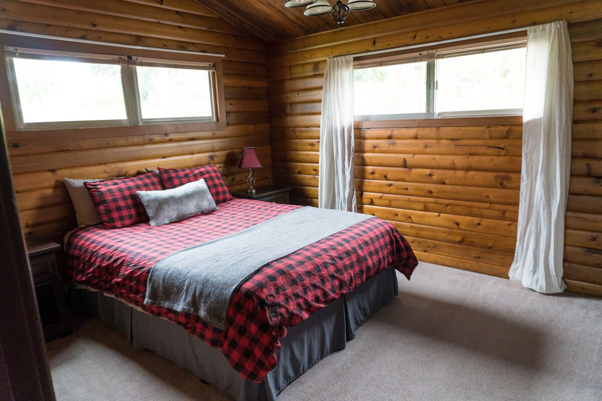 A wooden cabin bedroom with a bed, nightstands, and two windows with curtains.