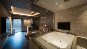 Ein modernes Badezimmer mit einer großen Badewanne, einer Duschkabine aus Glas und einem an der Wand befestigten Flachbildfernseher.