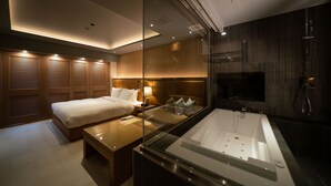 Ein modernes Hotelzimmer mit einem großen Bett, einer separaten Sitzecke, einer Glaskabinentubus und einer Wand aus Holzpaneelen.