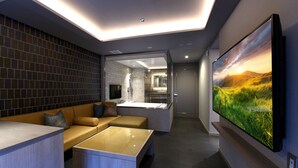 Ein modernes Wohnzimmer mit großem Flachbildfernseher, einer Couch, einem Couchtisch und einem ein Glasfenster umfassenden Badezimmer.