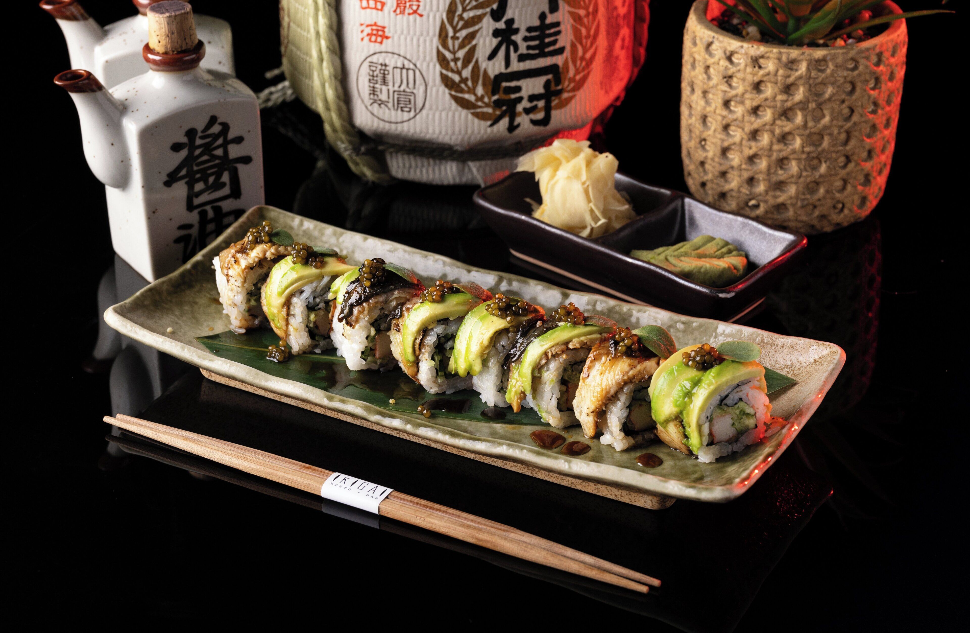A sushi platter on a ceramic plate with chopsticks beside it.