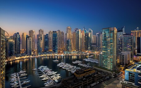 A marina with numerous boats docked, surrounded by high-rise buildings with illuminated windows.
