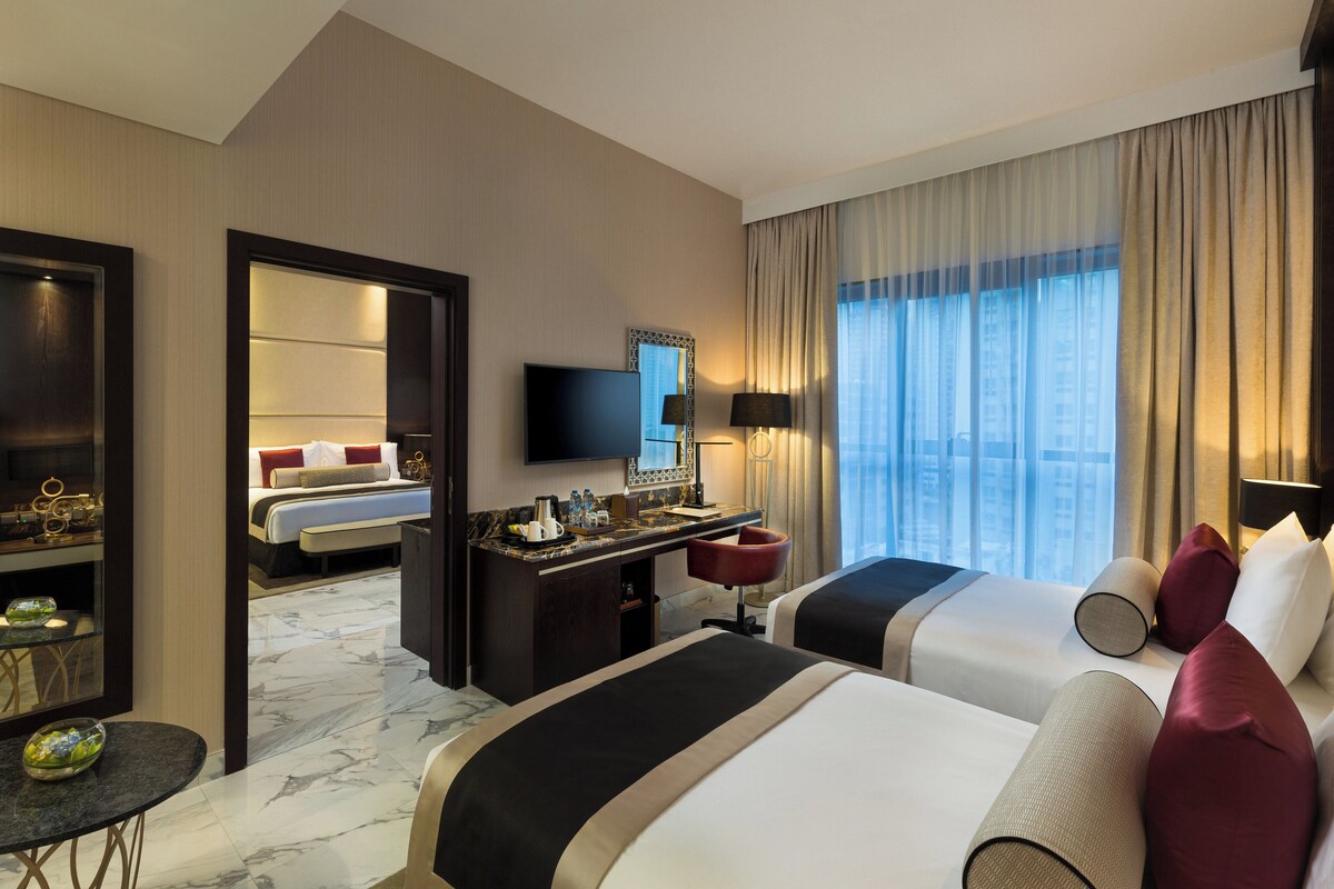 A hotel room with two beds, a desk, a TV, and a view of the city.