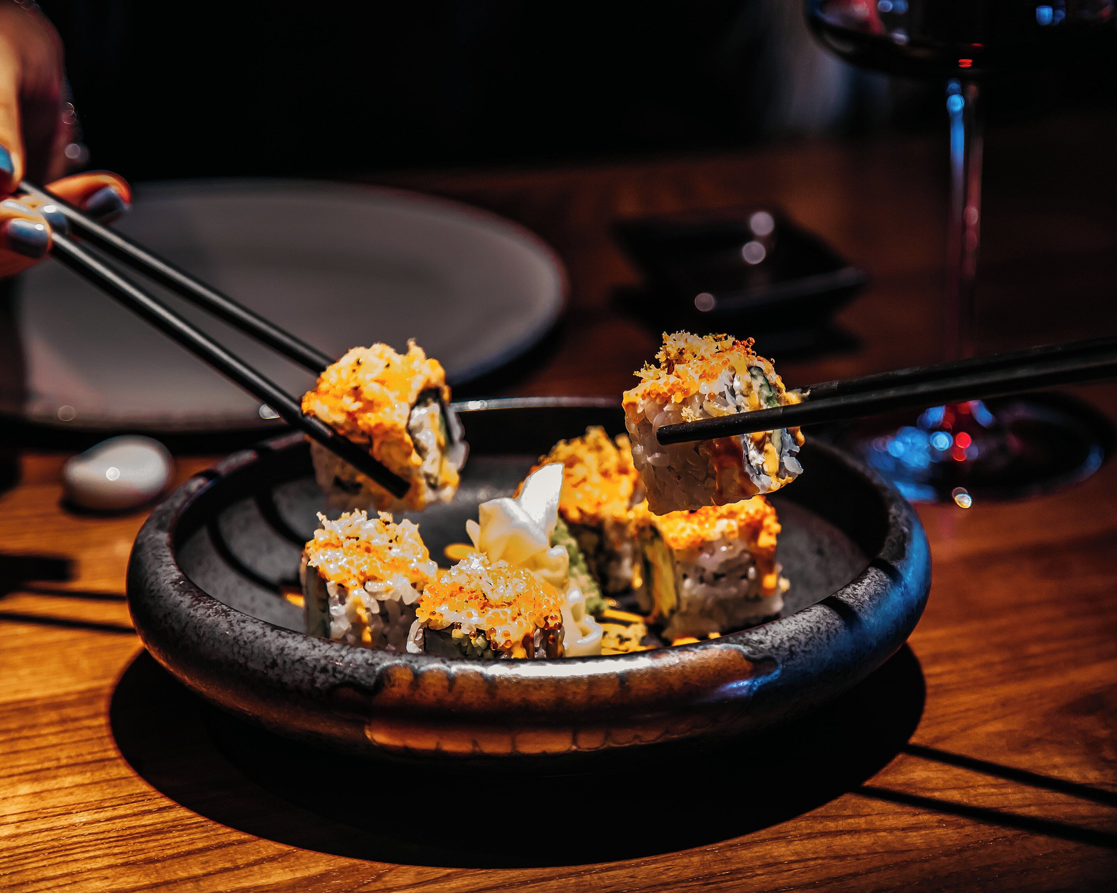 Sushi served on a black plate with chopsticks.