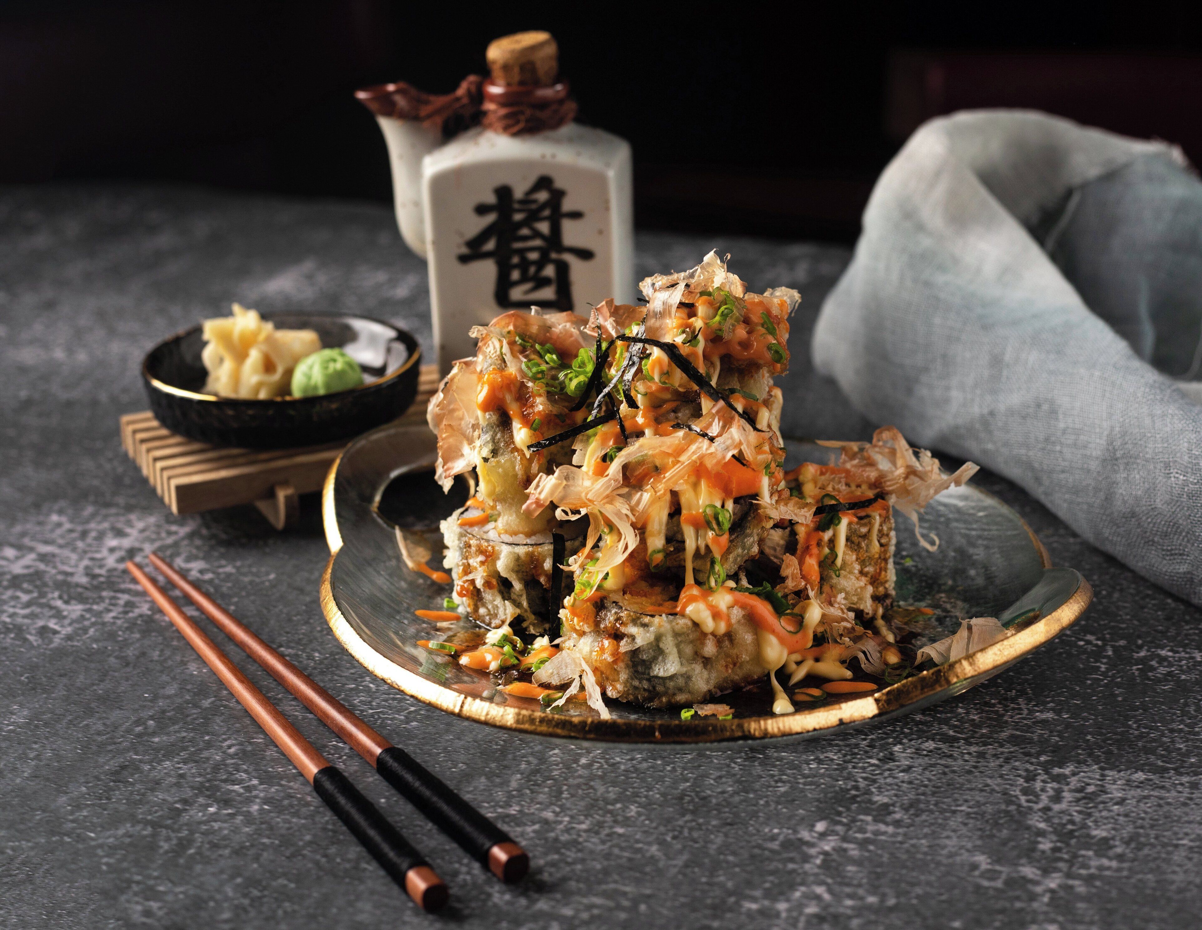 Tempura en un plat amb palets i un bol petit de te verd sobre una superfície fosca.