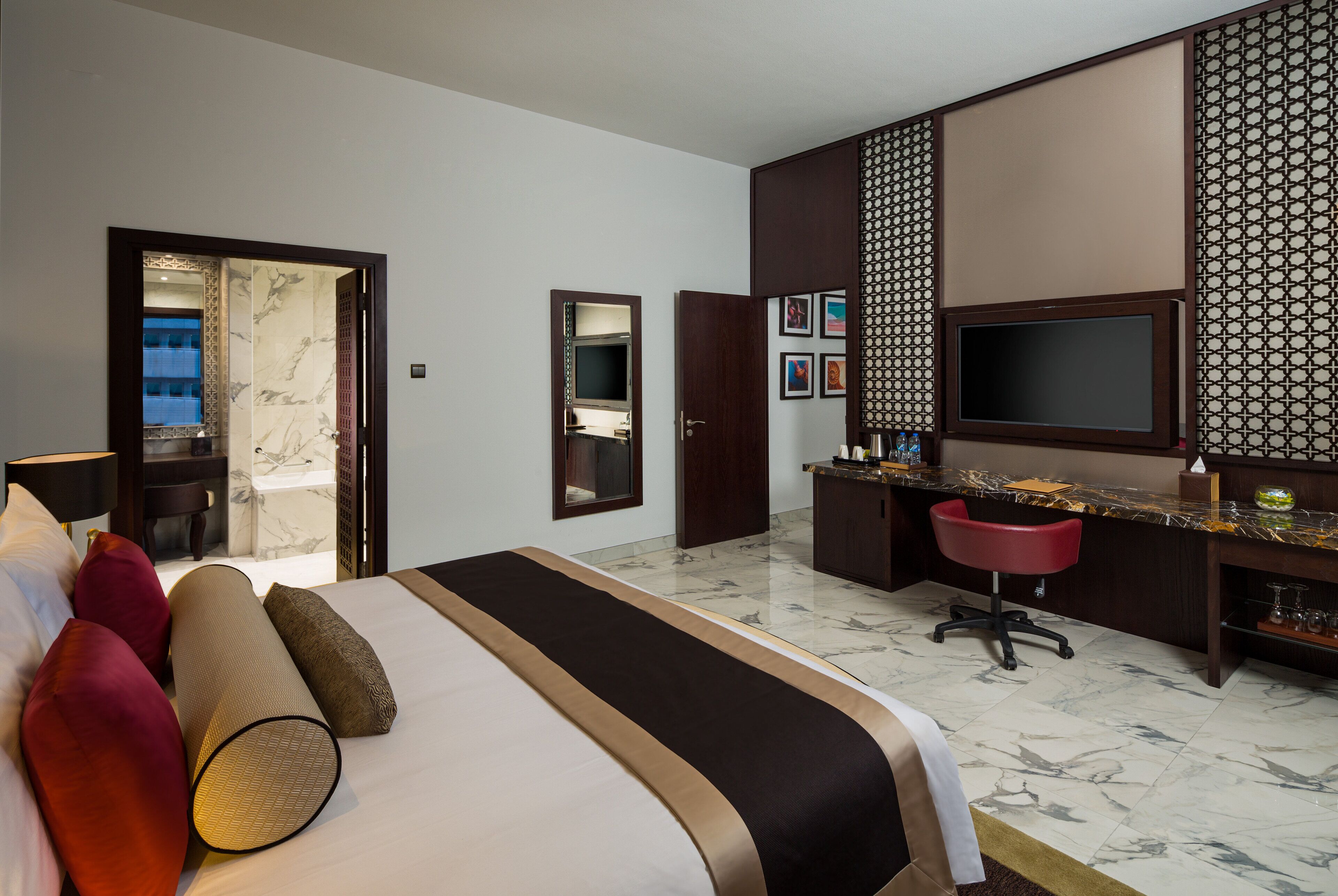 A hotel room with a bed, a desk, a chair, a TV, and a bathroom visible through an open door.