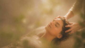 A person lying down with a hand gently touching their head, in a room with soft lighting and a blurred background.