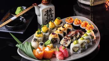 A variety of sushi on a plate, a bottle with Japanese characters, chopsticks, and a small bowl.