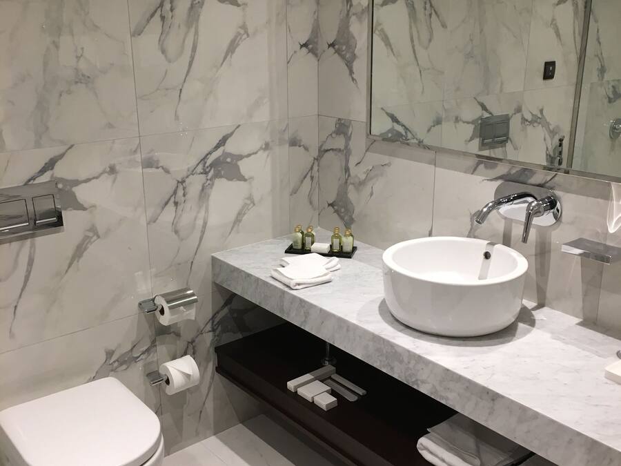 A modern bathroom with a white sink, marble walls, and a toilet.