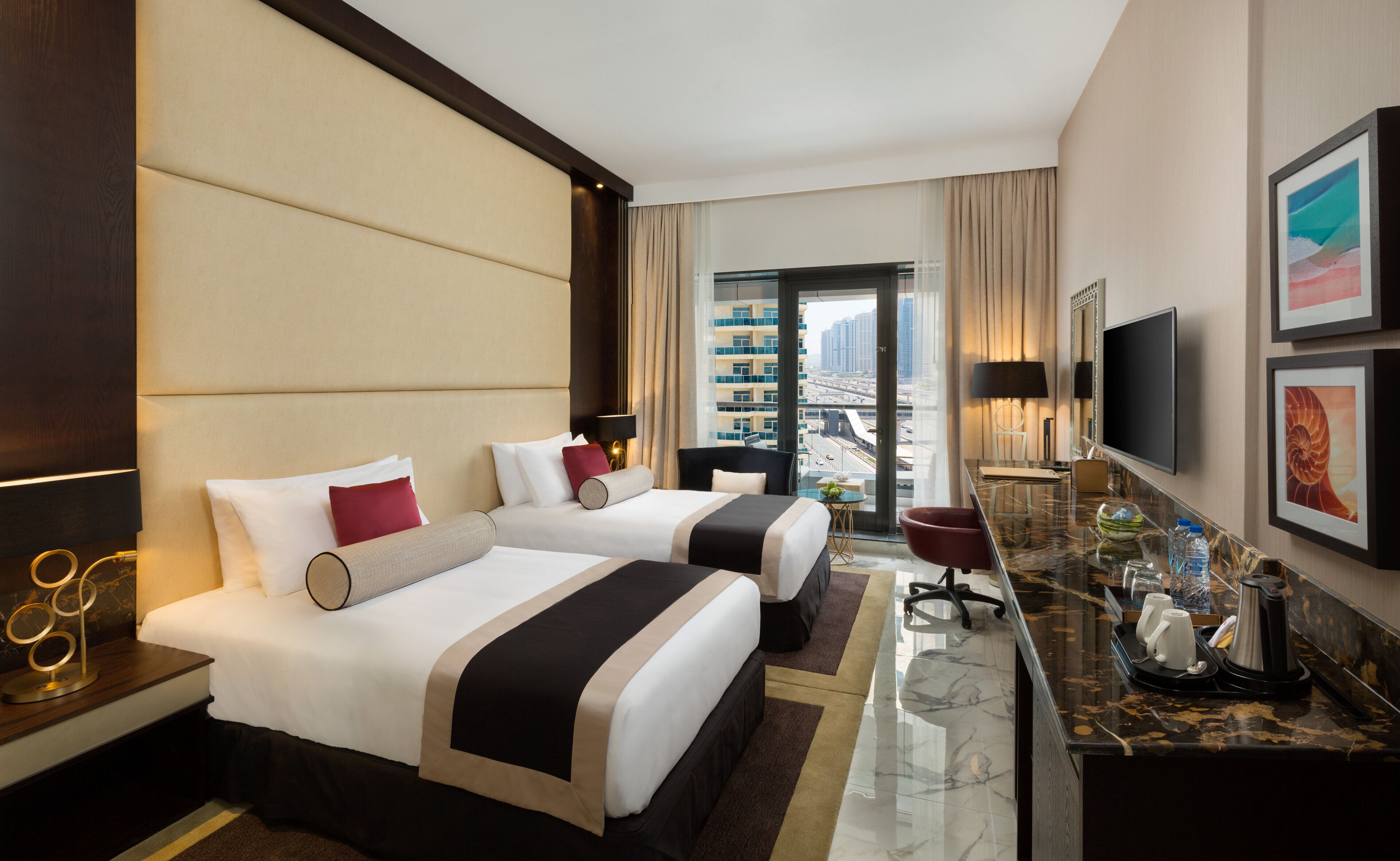 A hotel room with two beds, a desk with a coffee maker, a TV, and a view of the city.
