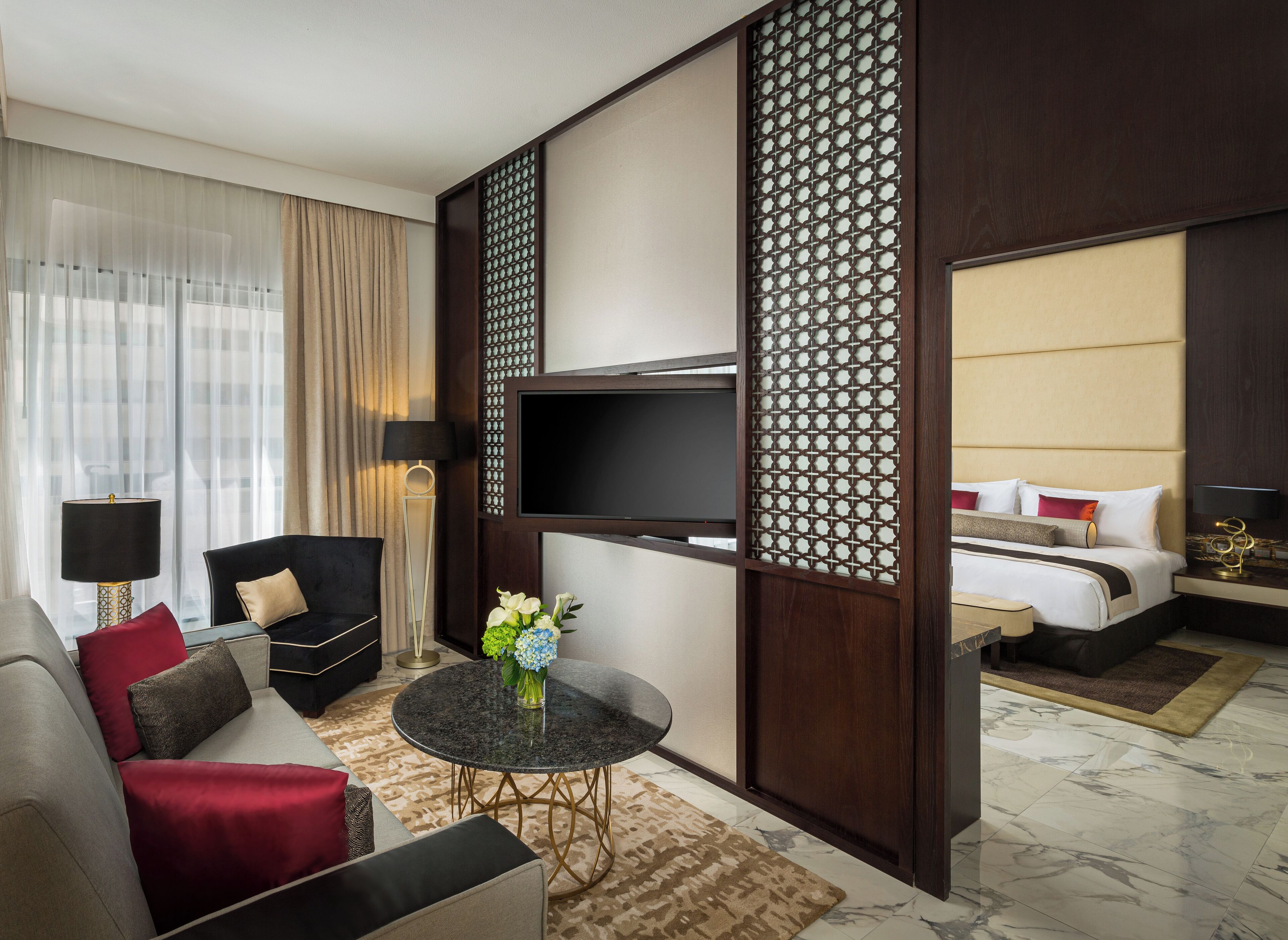 Een hotelkamer met een bank, fauteuil, ronde tafel, televisie en een bed met hoofdeinde.