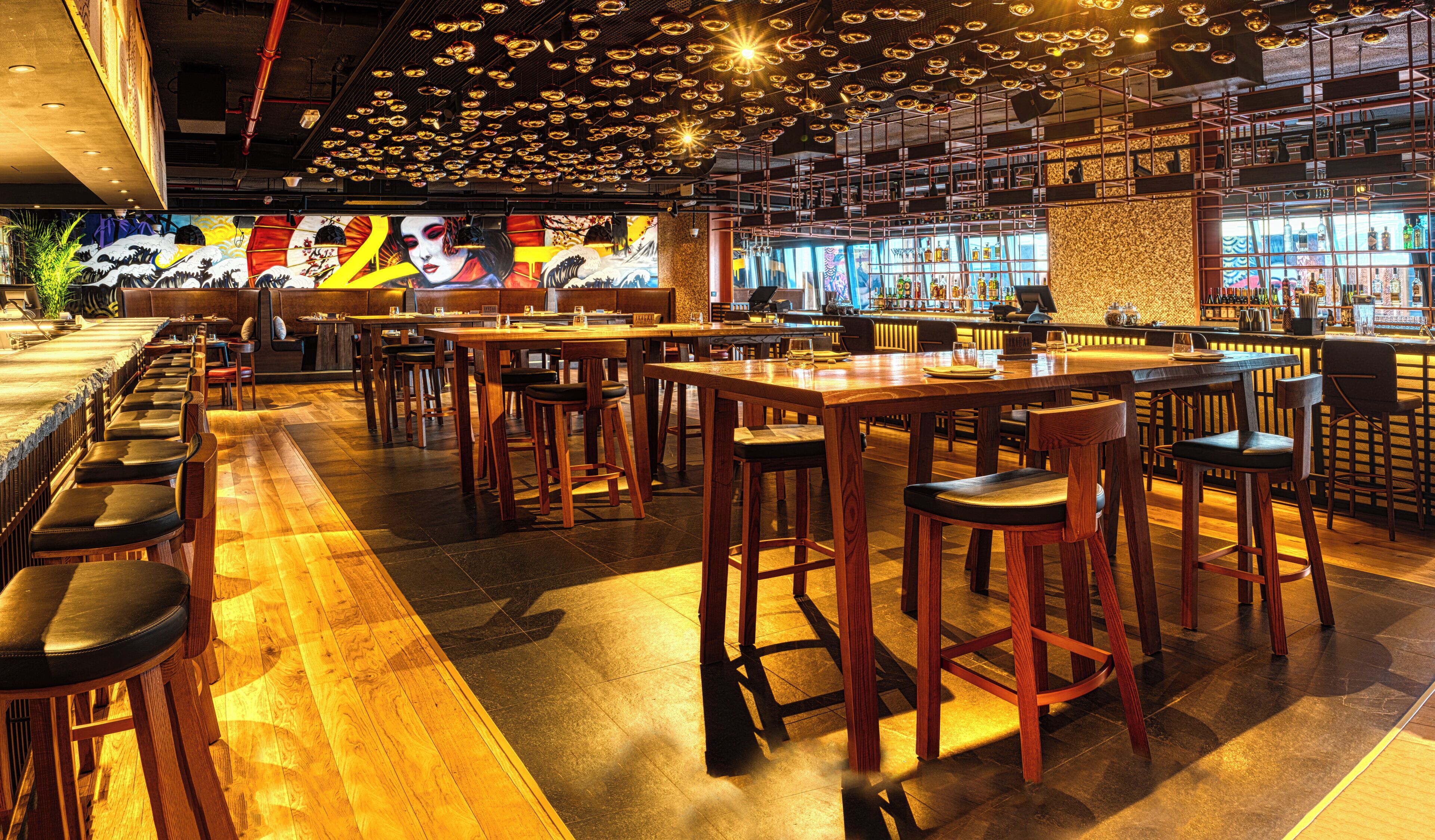 Un espace bar avec des tables et des chaises en bois, un comptoir de bar orné de bouteilles et une fresque murale.