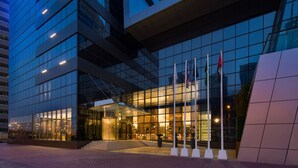 A modern hotel with a glass facade, a well-lit entrance, and multiple flags. - Millennium Place Marina (Dubai)