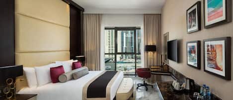 A modern hotel room with a large bed, a desk, a chair, a TV, and a view of the city.