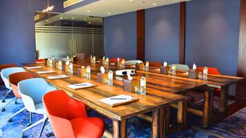 Un salón de conferencias con una larga mesa de madera, sillas coloridas y botellas de agua sobre la mesa.