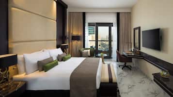 A hotel room with a large bed, a desk, a television, and a view of the city through the window.