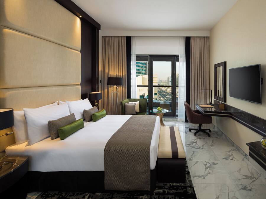 A hotel room with a large bed, a desk, a television, and a view of the city through the window.
