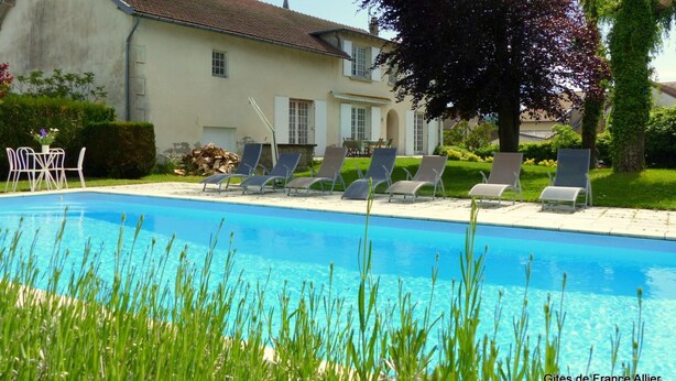 A swimming pool with lounge chairs, a building with a tiled roof, and a tree with purple leaves. - Spacious contemporary house with pool and pets allowed (Le Mayet-de-Montagne)