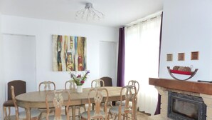 A dining room with a wooden table and chairs, a fireplace, and a painting on the wall. - Spacious contemporary house with pool and pets allowed (Le Mayet-de-Montagne)