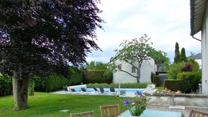 A backyard with a swimming pool, a covered patio table, and chairs. - Spacious contemporary house with pool and pets allowed (Le Mayet-de-Montagne)