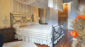 A bedroom with a bed, bedside tables, a nightstand, a lamp, and a decorative vase with flowers.