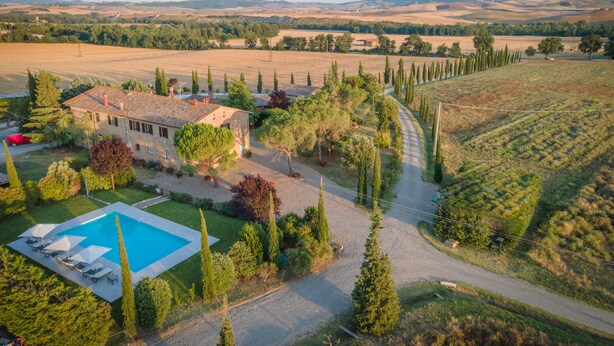 A large house with a swimming pool, surrounded by trees and fields.