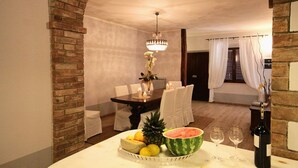 A dining area with a brick archway, a chandelier, a table set with white tablecloths, and a bowl of fruit and wine glasses.