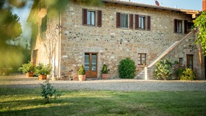 A stone building with a wooden door, multiple windows with shutters, and a gravel driveway.