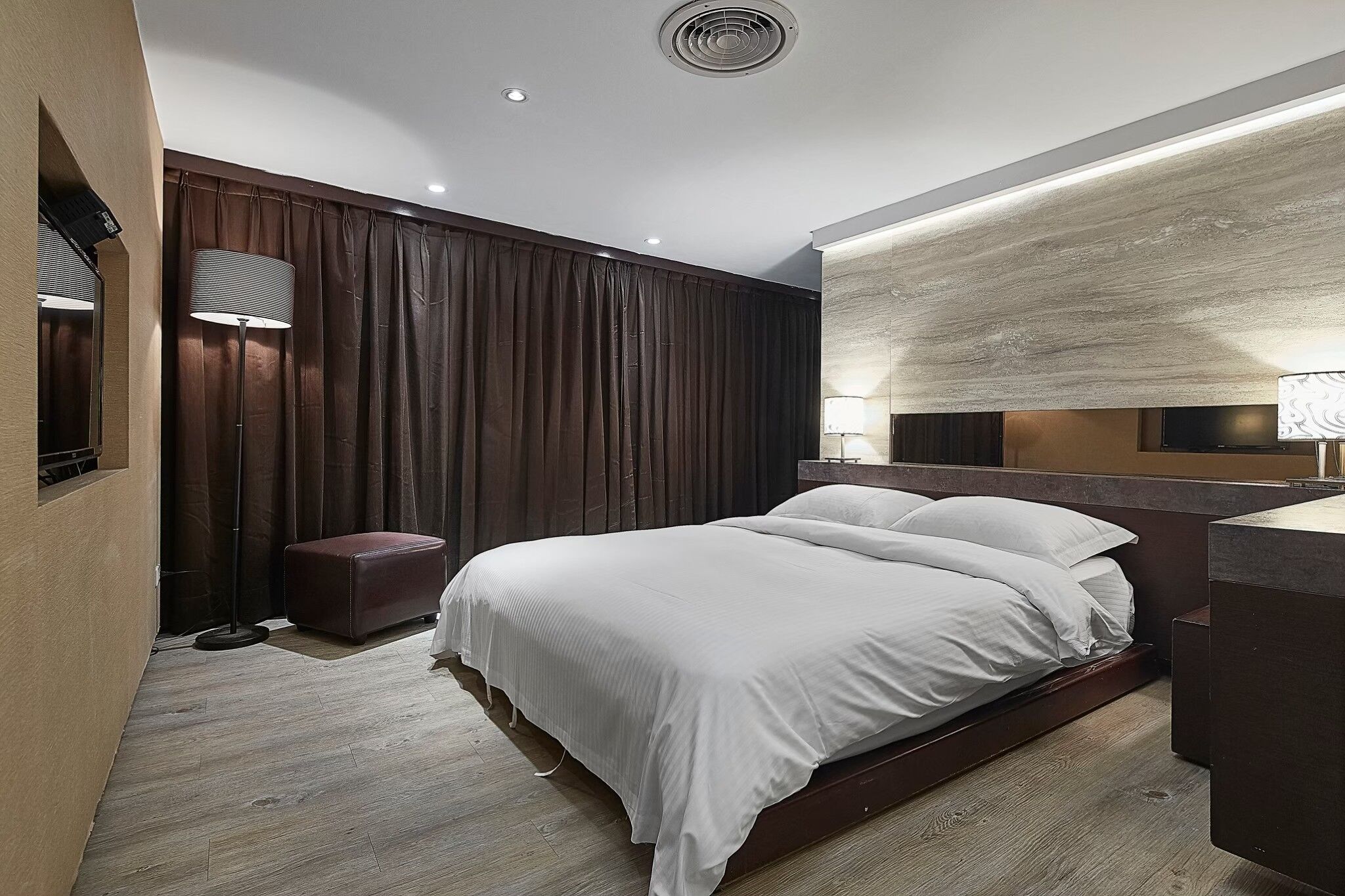 A modern hotel room with a large bed, a small seating area, and a large mirror.