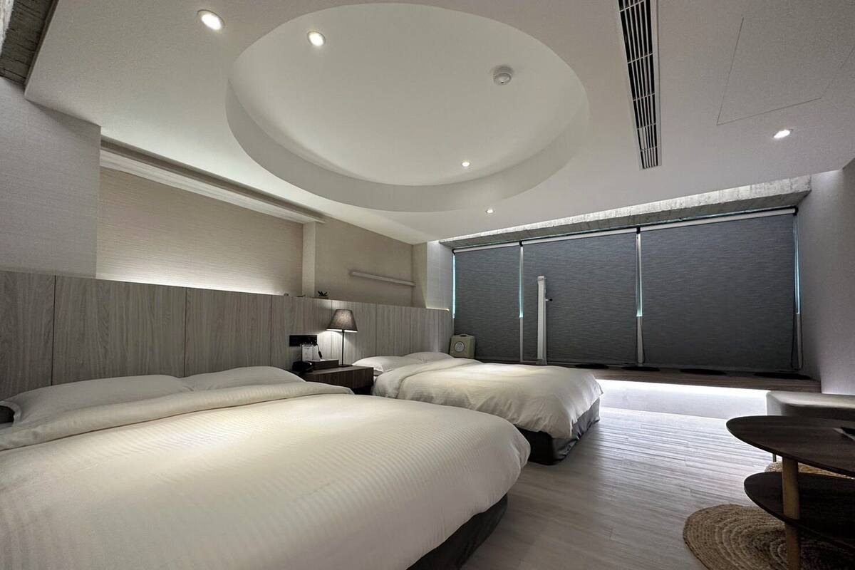 A modern hotel room with two large beds, a desk, and a large window.