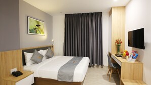 Habitación de hotel con cama, mesita de noche con teléfono, escritorio con silla, televisión y una ventana grande con cortinas.