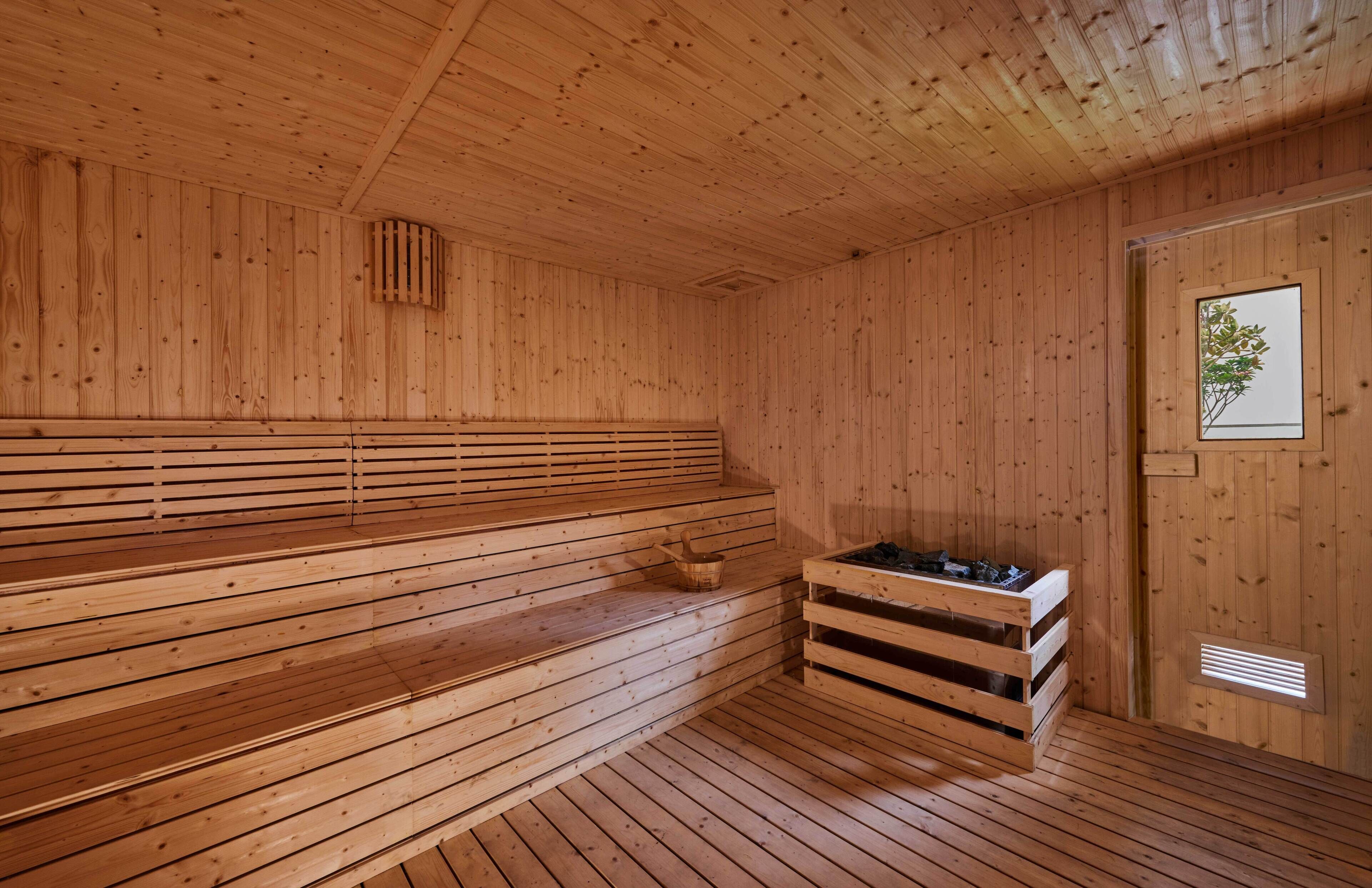 A wooden sauna with benches and a bench seat, a window, and a ventilation system.