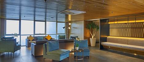 A modern lobby with a wooden ceiling, large windows, and seating areas with sofas and armchairs.