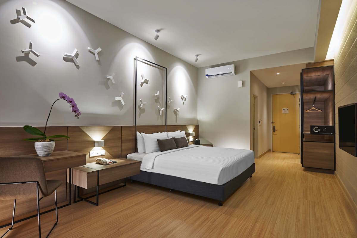 Ein modernes Hotelzimmer mit einem großen Bett, Nachttischen, einem Schreibtisch, einem Stuhl, einer Zimmerpflanze und einem Kleiderschrank.