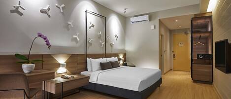 Ein modernes Hotelzimmer mit einem großen Bett, Nachttischen, einem Schreibtisch, einem Stuhl, einer Zimmerpflanze und einem Kleiderschrank.