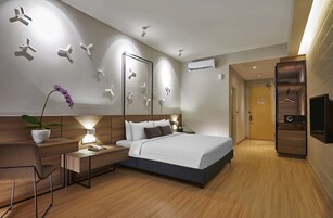 Moderni hotellihuone, jossa on suuri sänky, yöpöydät, työpöytä, tuoli, ruukkukasvi ja vaatekaappi.