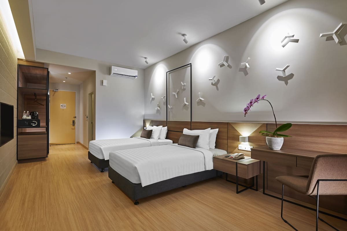 Ein Hotelzimmer mit zwei Betten, einem Schreibtisch, einem Stuhl, einem Fernseher und einem wandmontierten Spiegel.
