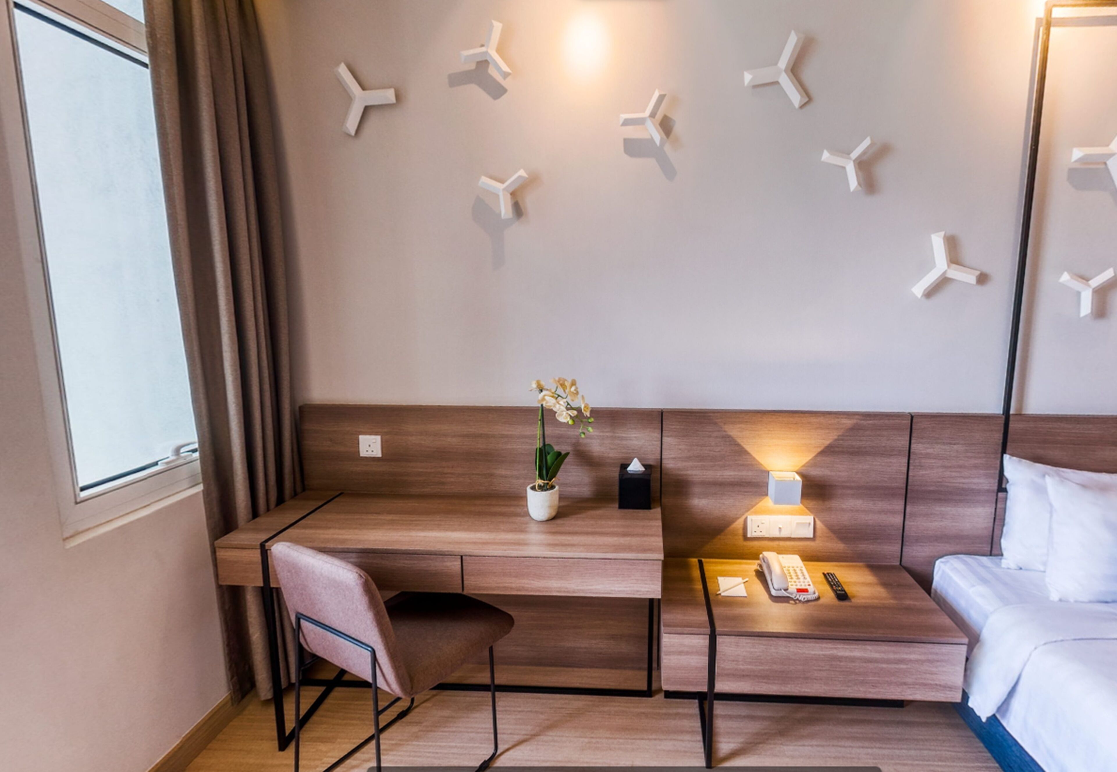 Une chambre d’hôtel avec un bureau en bois, une chaise, une table de chevet avec une lampe, un téléphone et un lit.