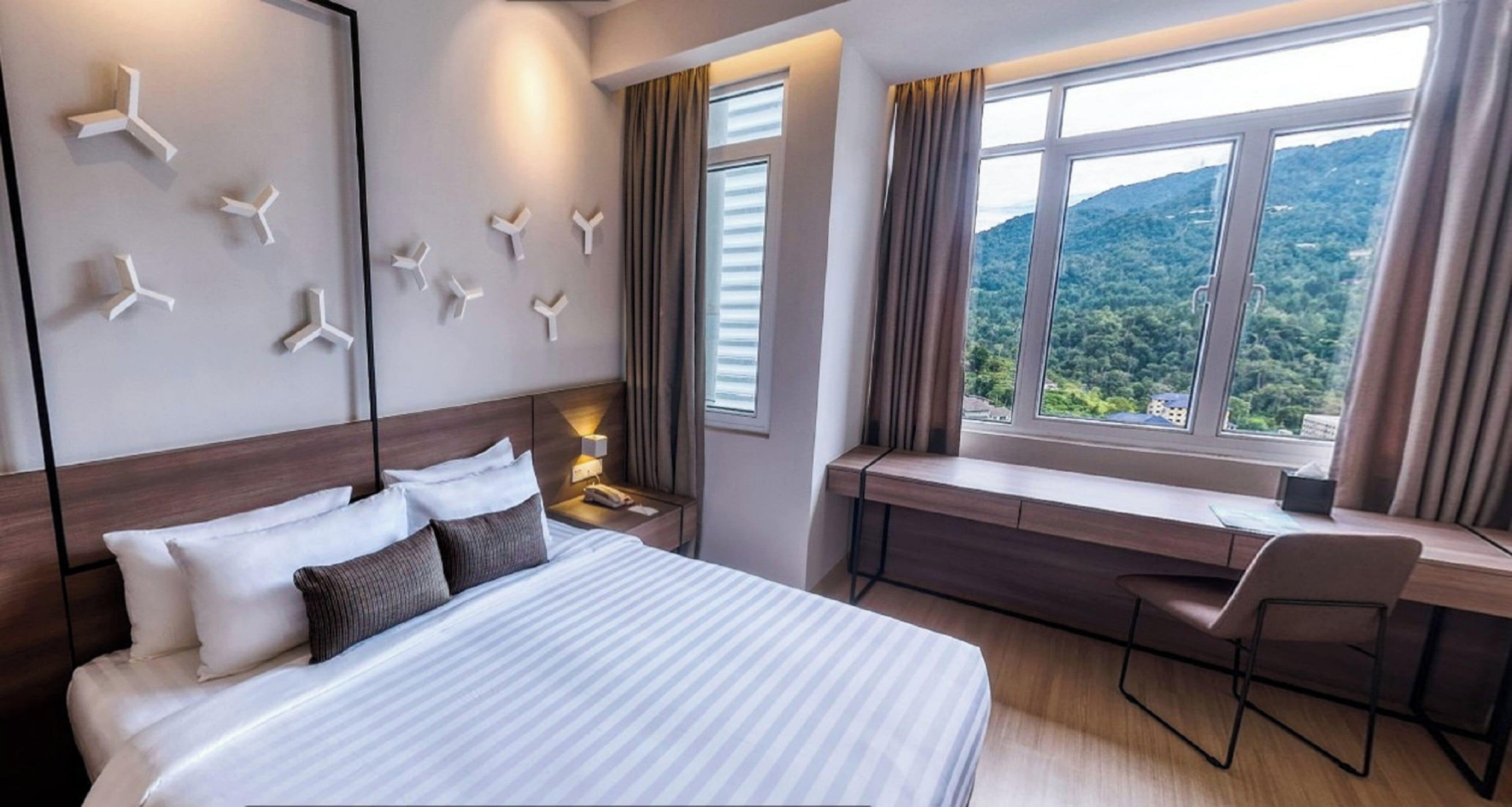 A hotel room with a bed, a desk, a chair, a nightstand, and a window with a view of the outdoors.