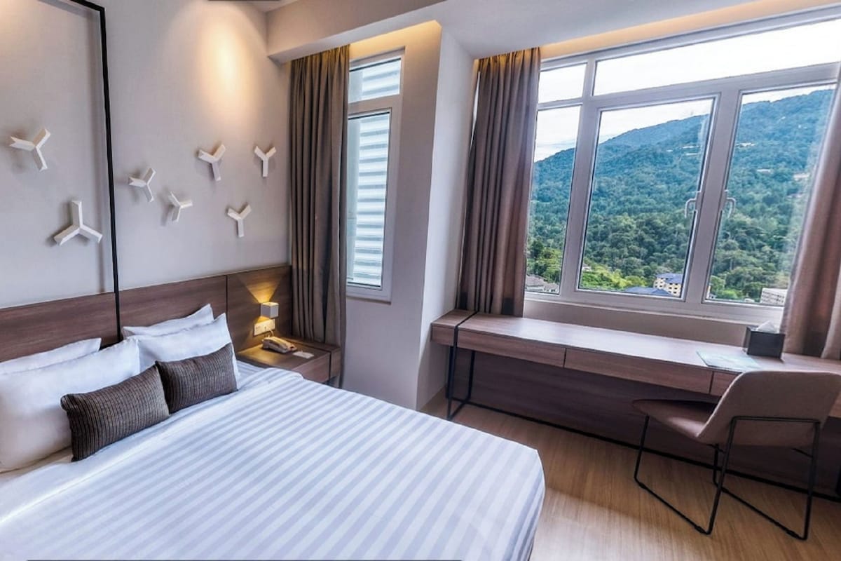 Ein Hotelzimmer mit einem großen Bett, einem Schreibtisch mit Stuhl, Blick ins Freie und Wandbildern.