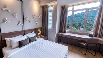 A hotel room with a bed, a desk, a chair, a nightstand, and a window with a view of the outdoors.