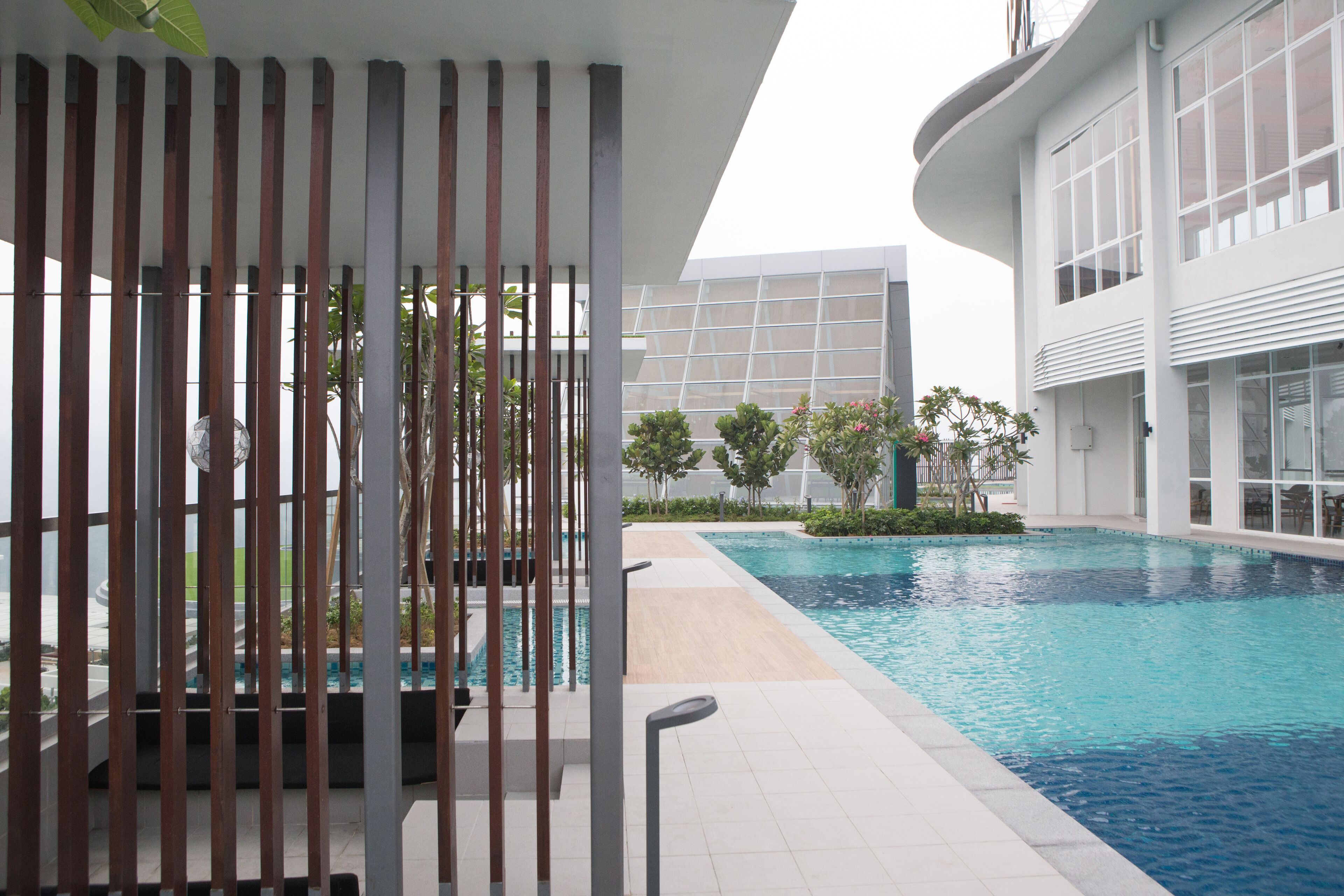A modern pool area with a clear view of the pool, surrounding greenery, and a contemporary building structure.