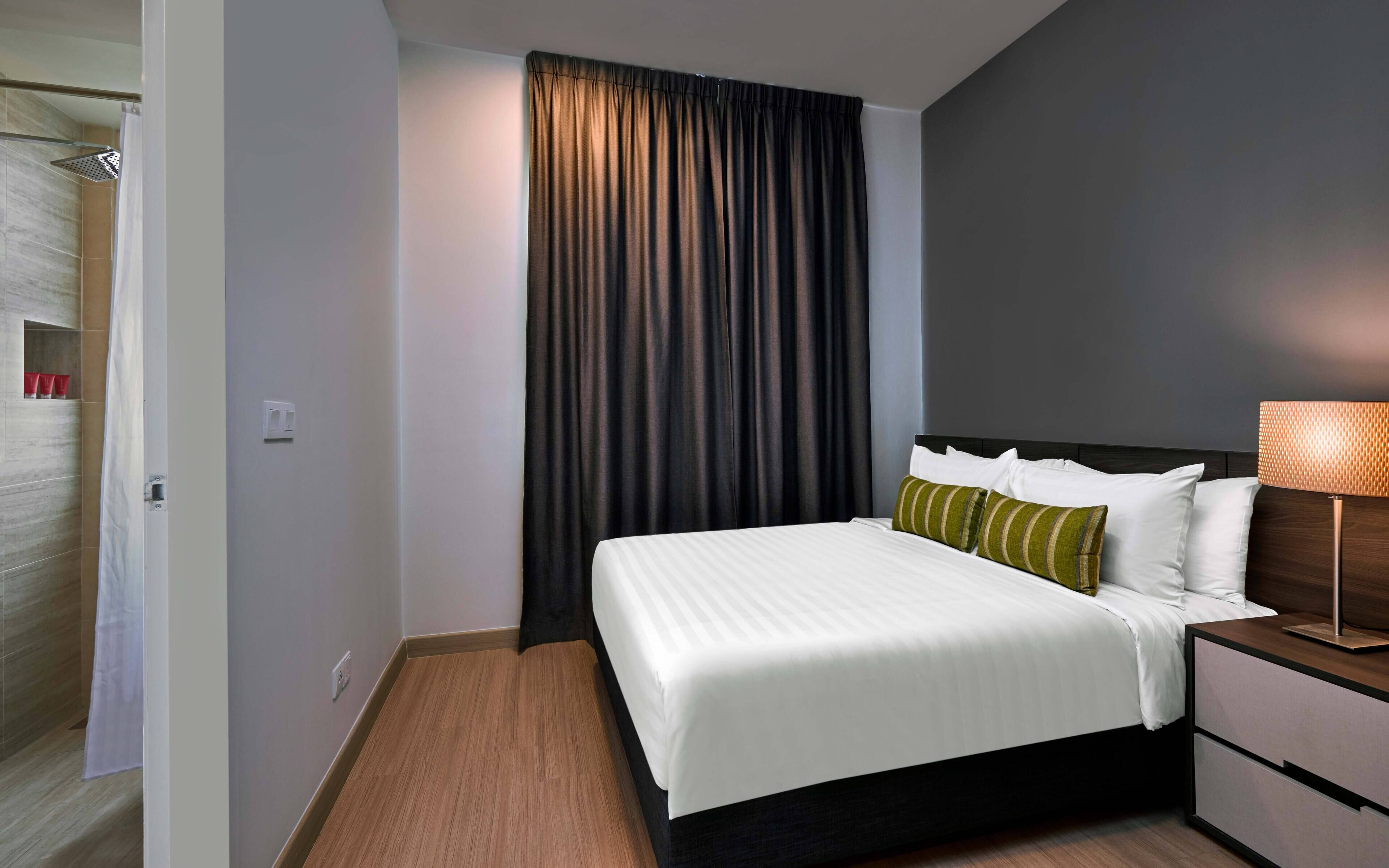 A hotel room with a bed, a nightstand, a lamp, and a shower area.
