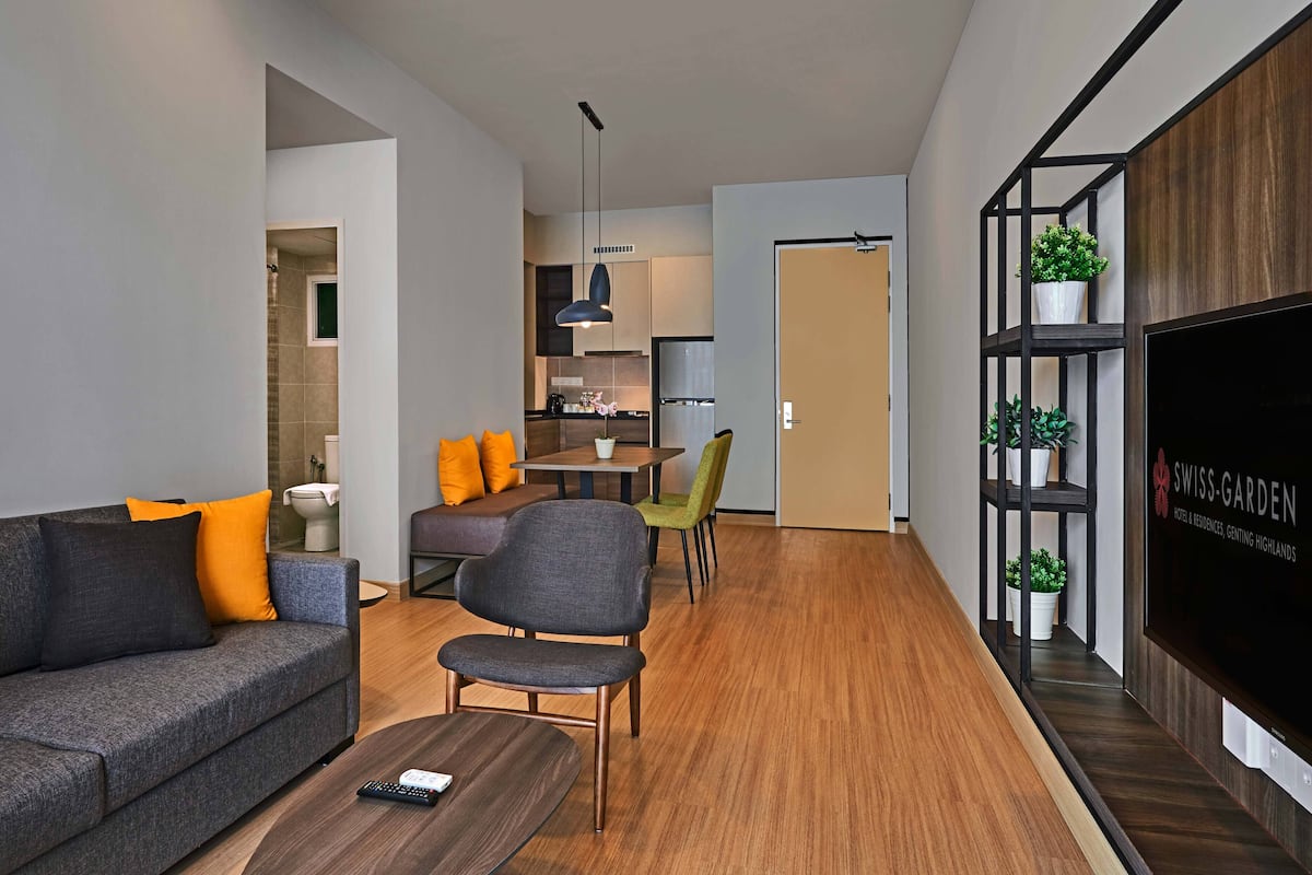 Ein modernes Wohnzimmer mit Sofa, Sessel und Couchtisch. Ein Fernseher ist an der Wand angebracht und es gibt Holzdielenboden.
