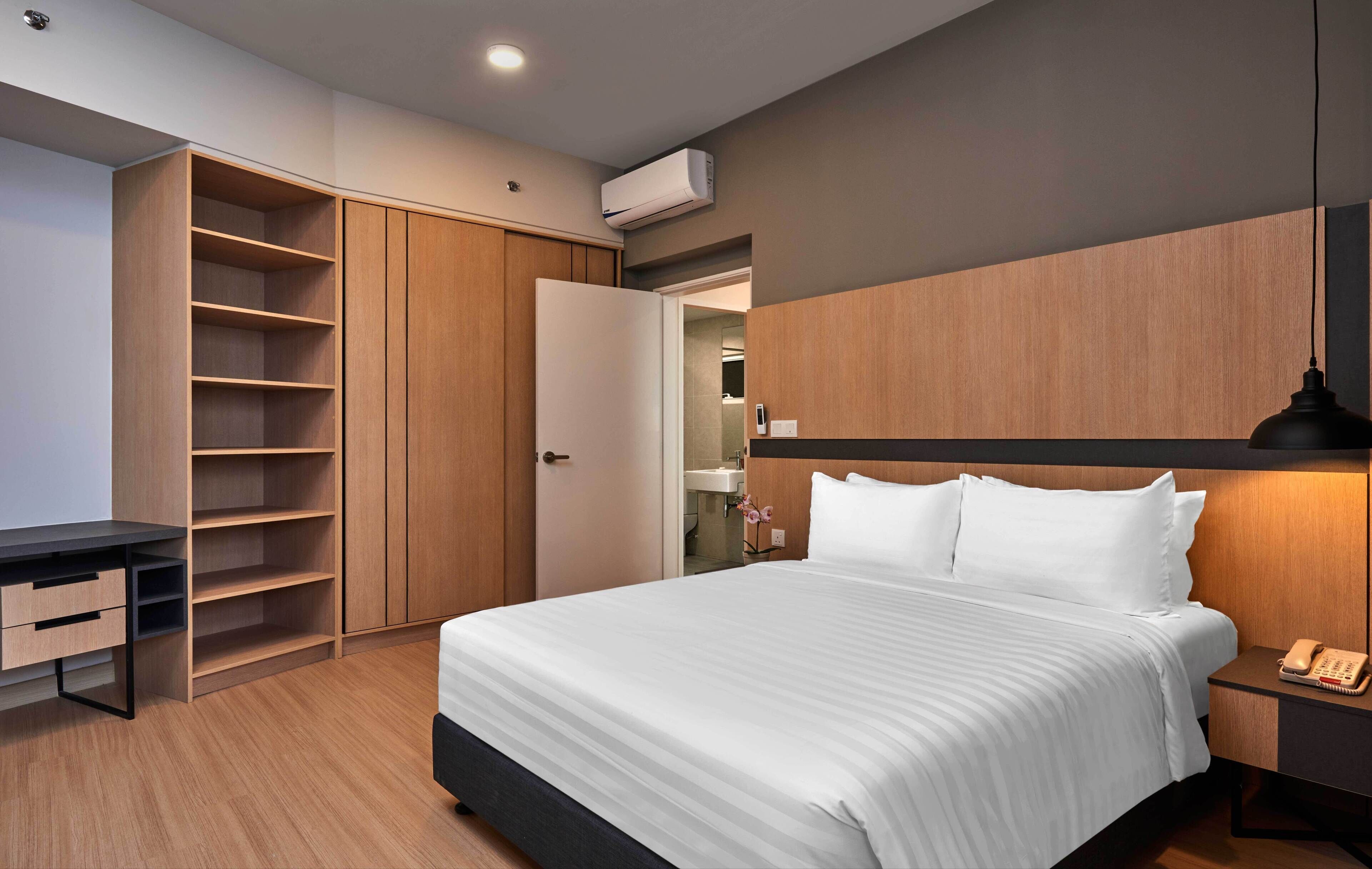 A modern bedroom with a large bed, a desk, and a wardrobe.